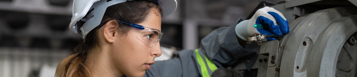 Female maintenance technician in safety uniform and helmet diligently checking and maintaining a robotic arm machine at a high-tech manufacturing factory, ensuring optimal performance and safety standards.