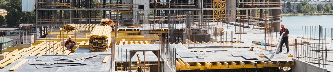 A bustling construction site with multiple cranes and workers. The scene includes various construction equipment and materials, with workers wearing safety gear such as helmets and vests. The background shows partially constructed buildings and scaffolding, indicating ongoing development. Contact Aerotek to learn more about employee performance monitoring solutions. 