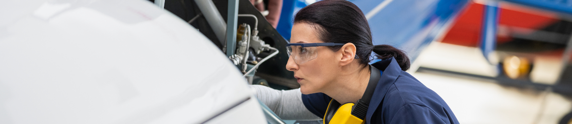 Female aircraft mechanic with a digital tablet, meticulously inspecting and working on a helicopter inside a hangar. The setting conveys a theme of safety and precision in aviation maintenance