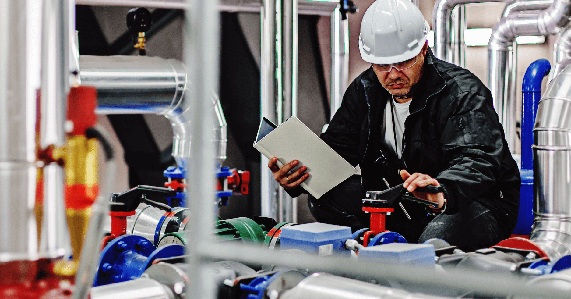 A worker in a jacket and wearing a hard hat works on a system.